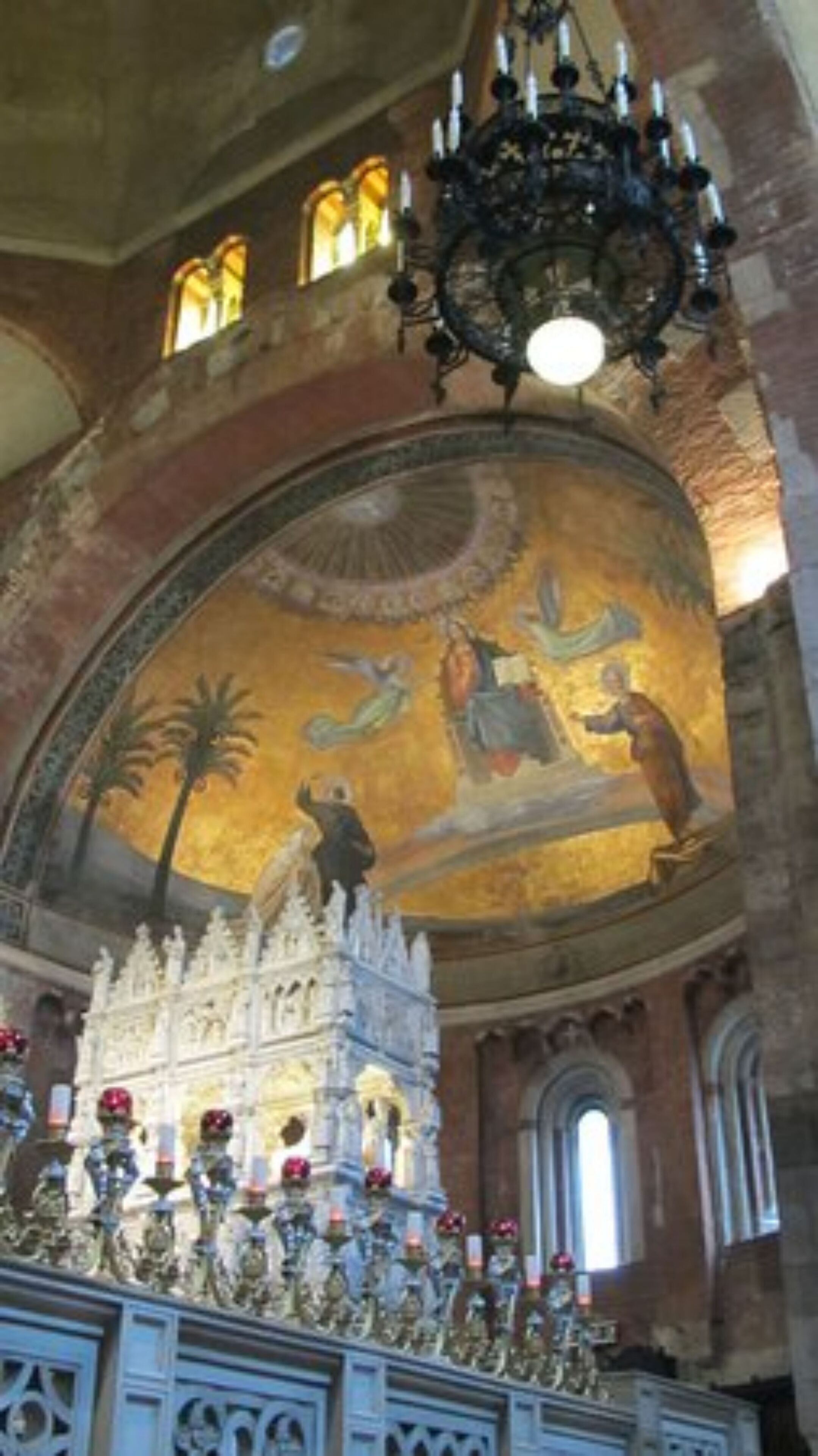 An ornate church interior with a large mosaic on the ceiling, a chandelier, and a detailed altar.
