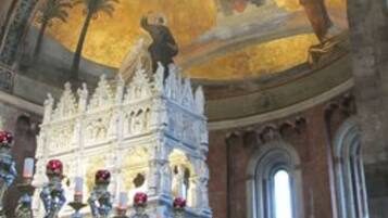 An ornate church interior with a large mosaic on the ceiling, a chandelier, and a detailed altar.