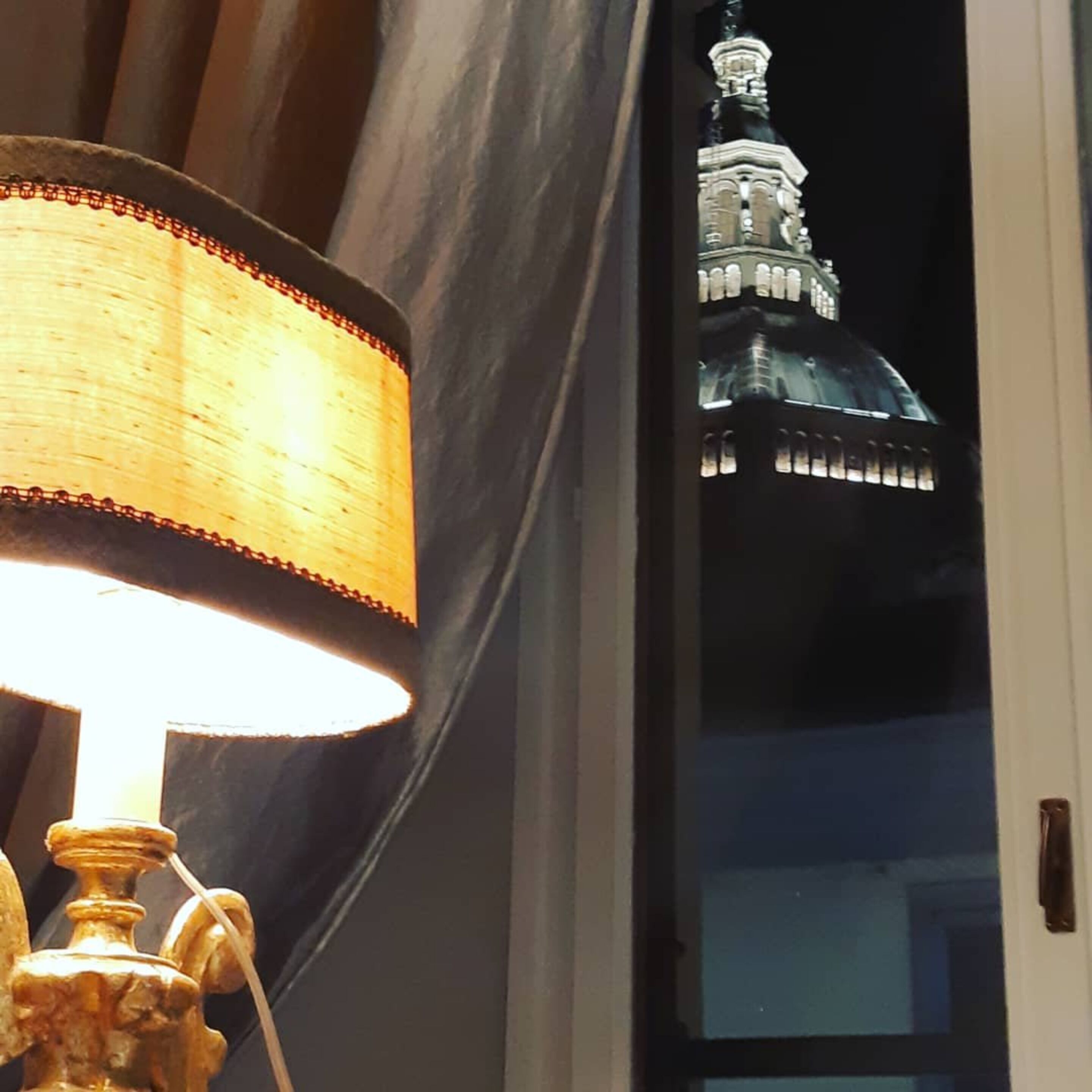 En lampa med en beige lampskärm och en guldfärgad fot, placerad framför ett fönster.