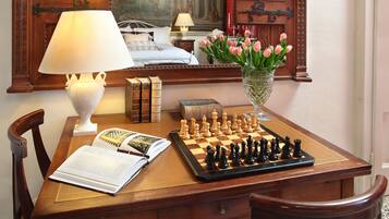 A wooden desk with a chessboard, books, a lamp, and a vase with flowers.