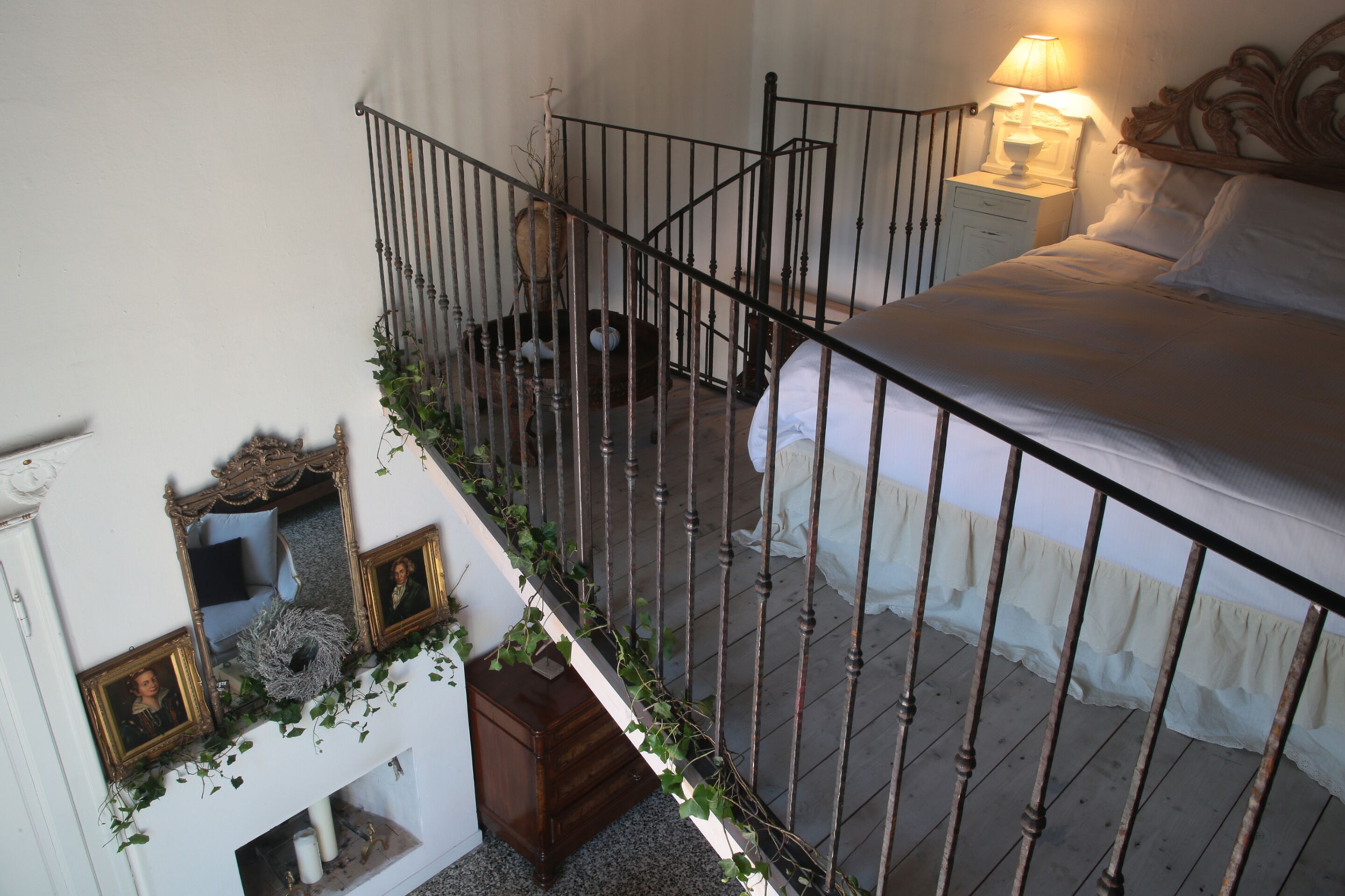 A bedroom with a bed, a nightstand, a lamp, a wooden headboard, and a staircase with a railing.