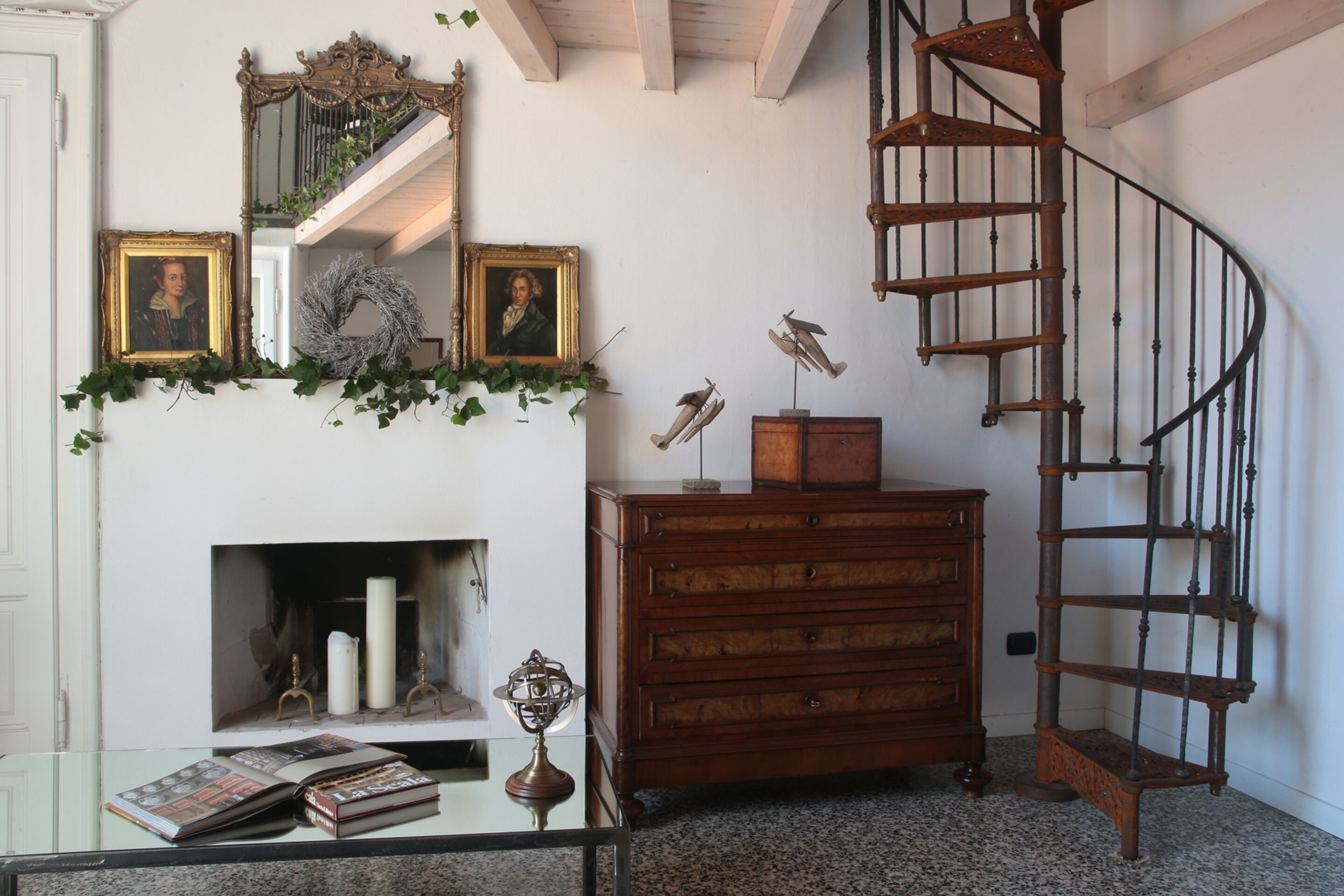 A room with a fireplace, wooden dresser, and a spiral staircase.