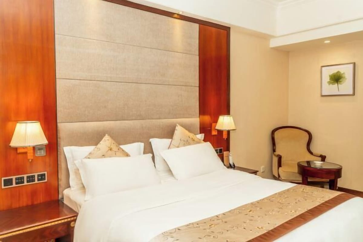 A hotel room with a large bed, two bedside lamps, a chair, and a small table.
