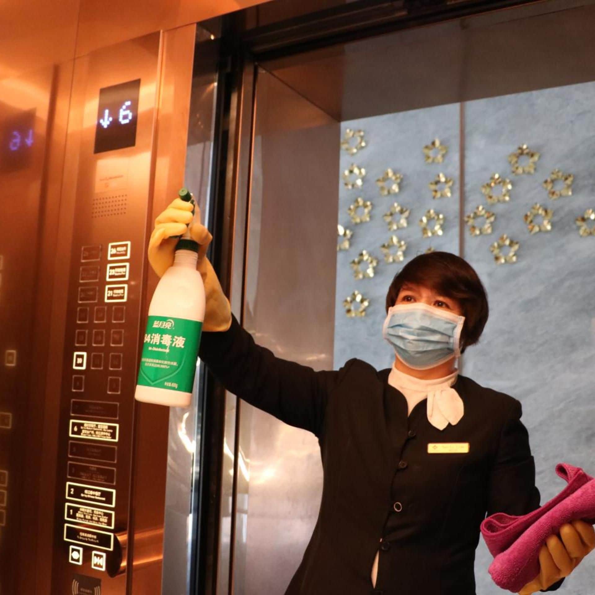 A person holding a bottle of cleaning solution and a cloth inside an elevator.