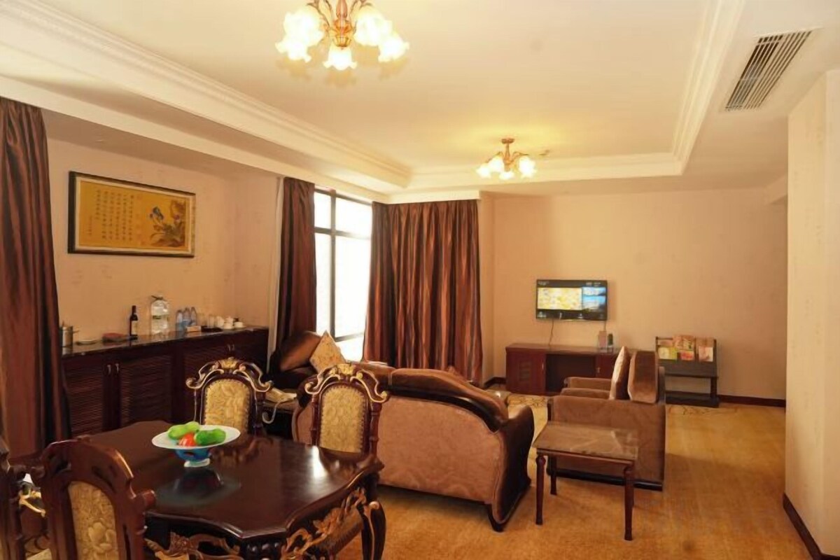 A hotel room with a dining table, chairs, a sofa, a television, and a decorative wall piece.