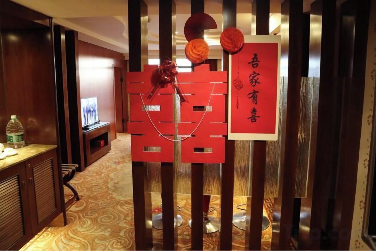 A hotel corridor with a reception desk, a television, and a decorative red structure with a sign.