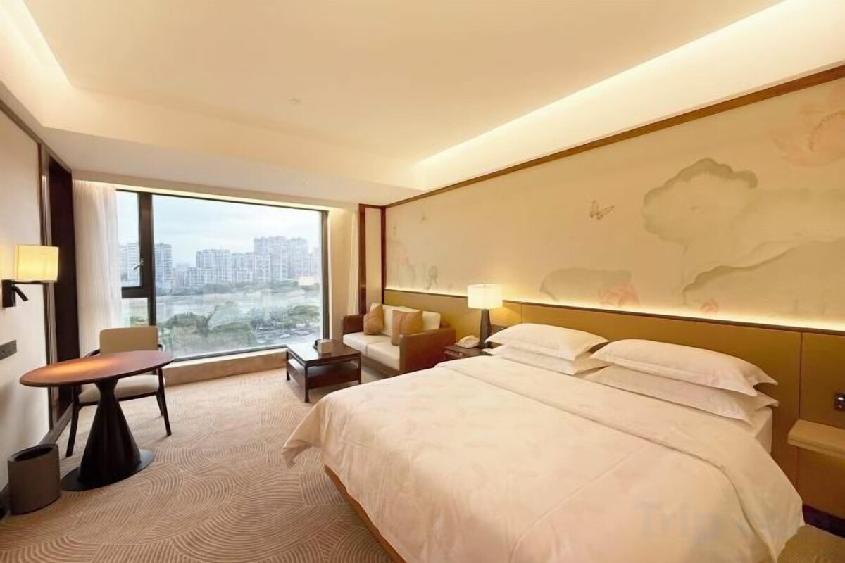 A hotel room with a large bed, a desk, a chair, and a view of the city.