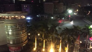 A nighttime cityscape with a prominent circular building with illuminated windows, palm trees, and streetlights. - Rongjiang Hotel (Jieyang)
