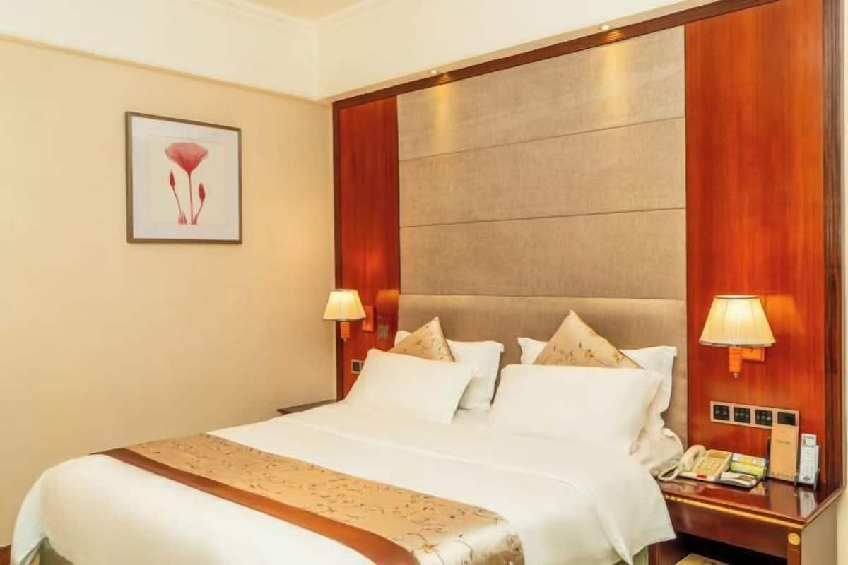 A hotel room with a large bed, two bedside lamps, a telephone, and a framed picture on the wall.