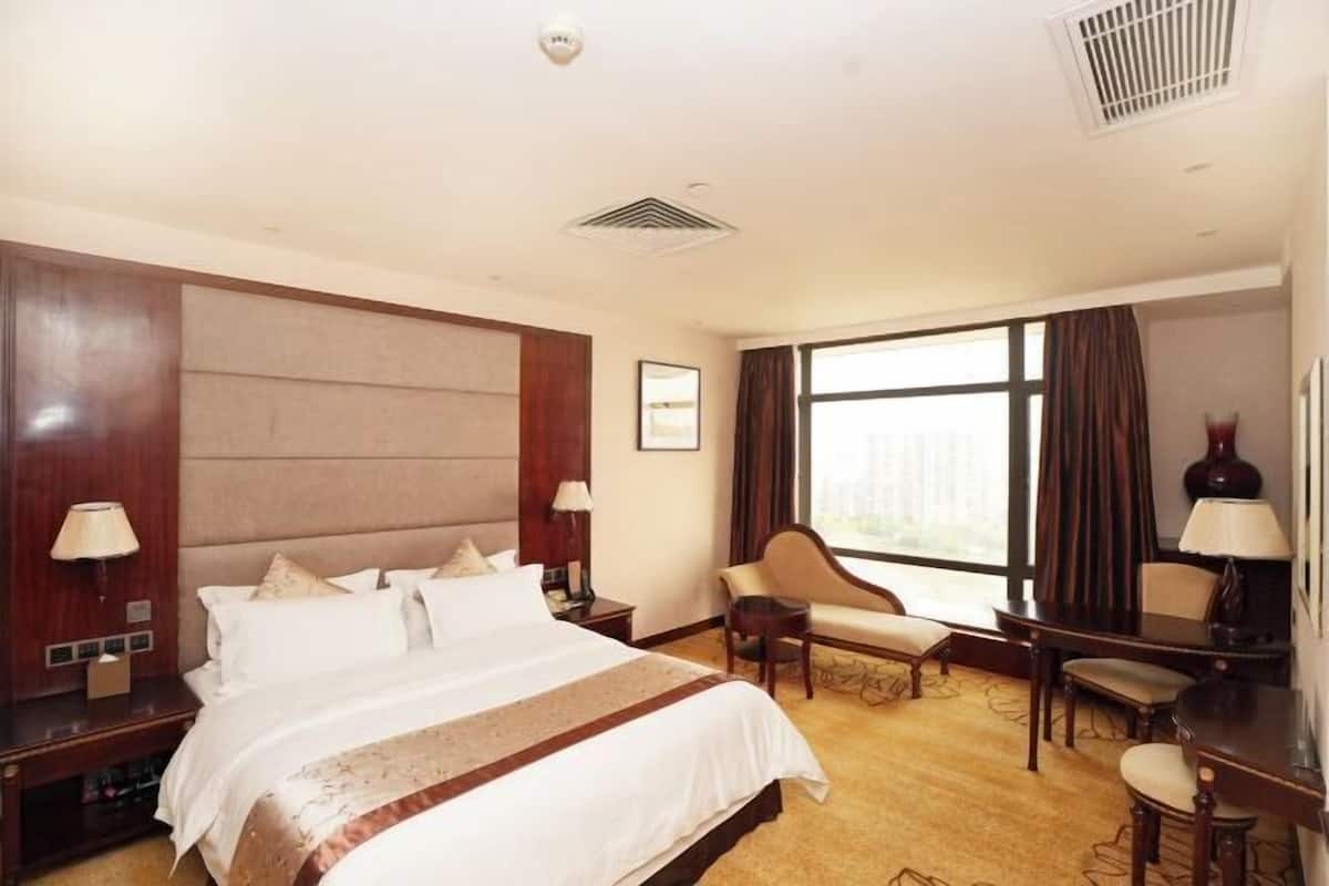 A hotel room with a large bed, a desk, a chair, and a sofa.