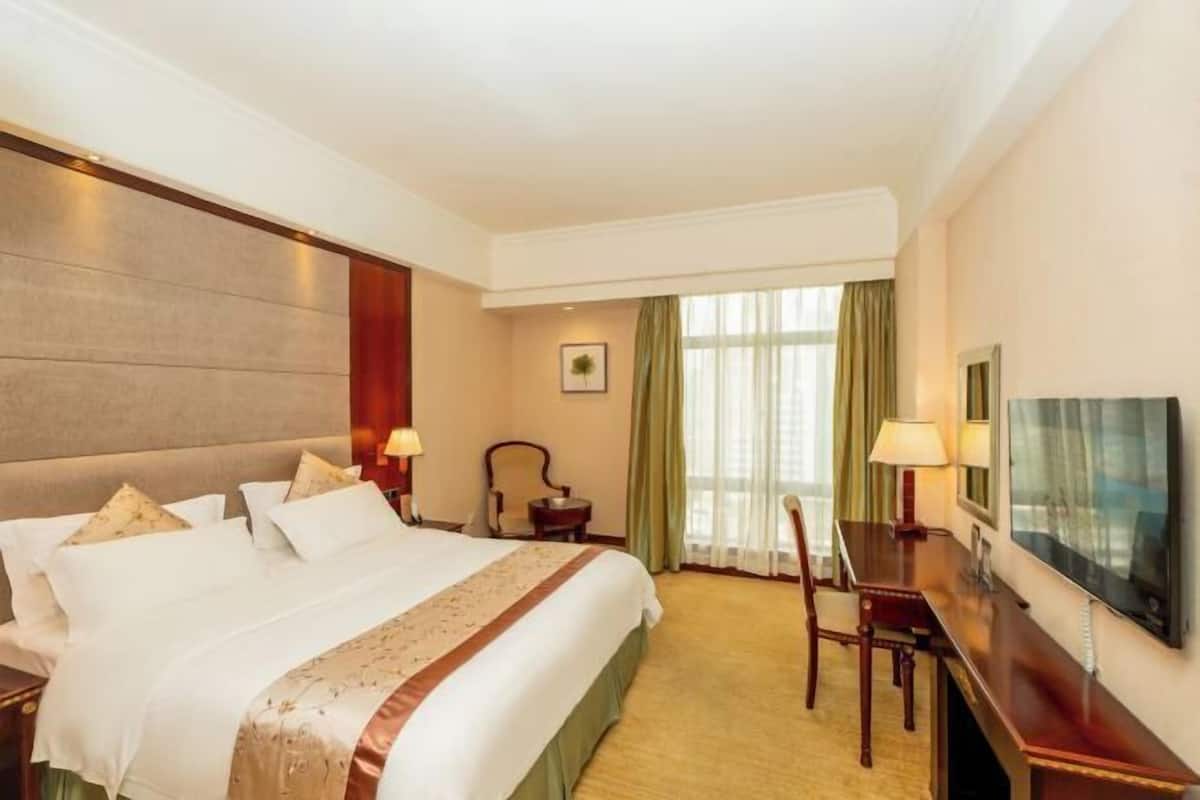 A hotel room with a large bed, a desk, a chair, a TV, and a window with curtains.