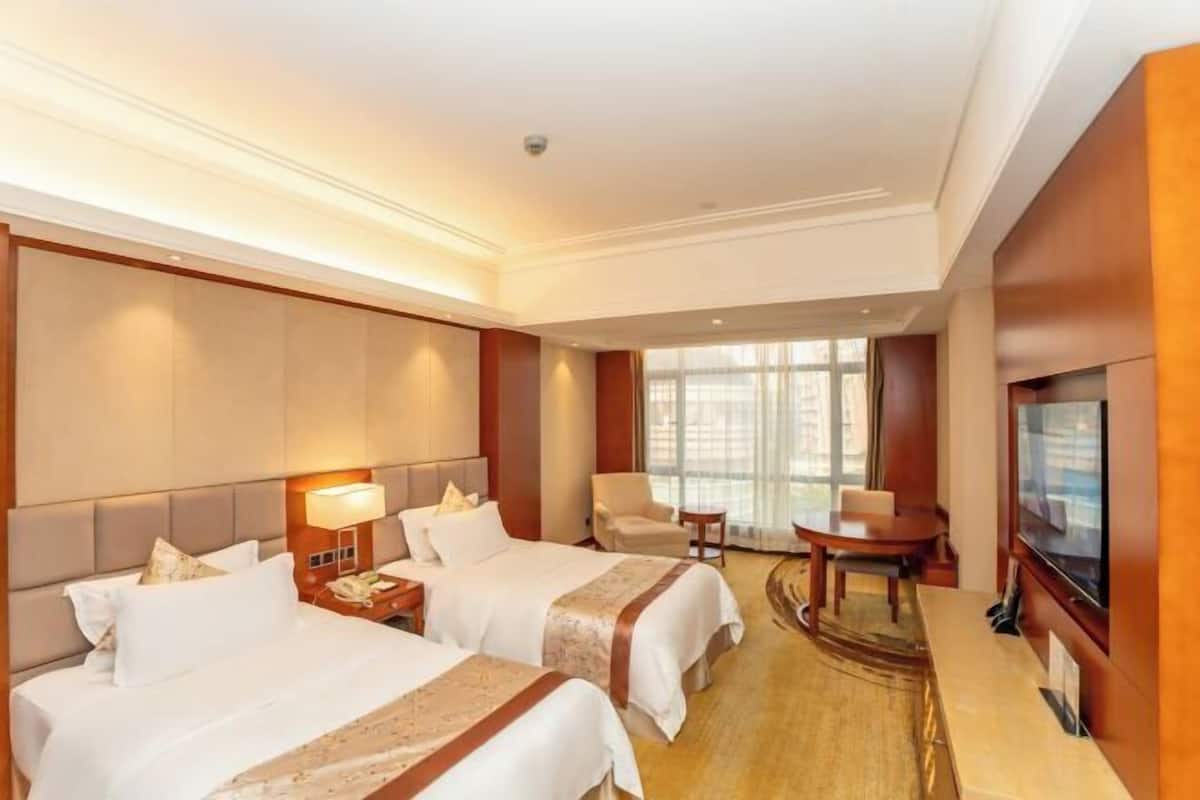 A hotel room with two beds, a TV, a desk, and a chair.