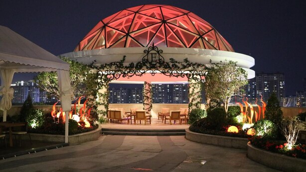 A dome-shaped structure with a white canopy and seating area, surrounded by decorative plants and fire features. - Rongjiang Hotel (Jieyang)