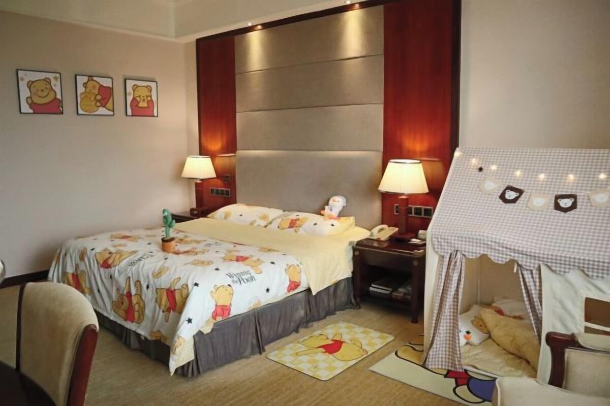 A hotel room with a bed, bedside tables, a lamp, a tent-like structure, and Winnie the Pooh-themed decor.