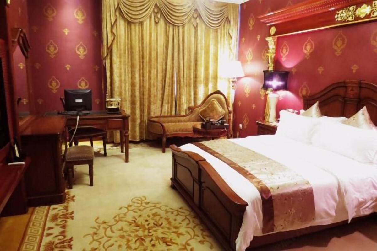 A hotel room with a bed, a desk, a chair, a lamp, and a curtain.
