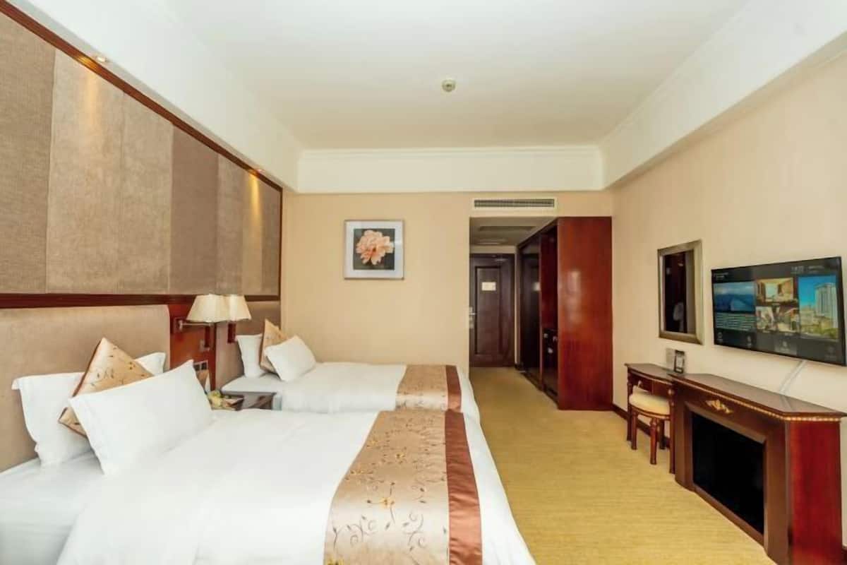 A hotel room with two beds, a desk, a television, and a fireplace.