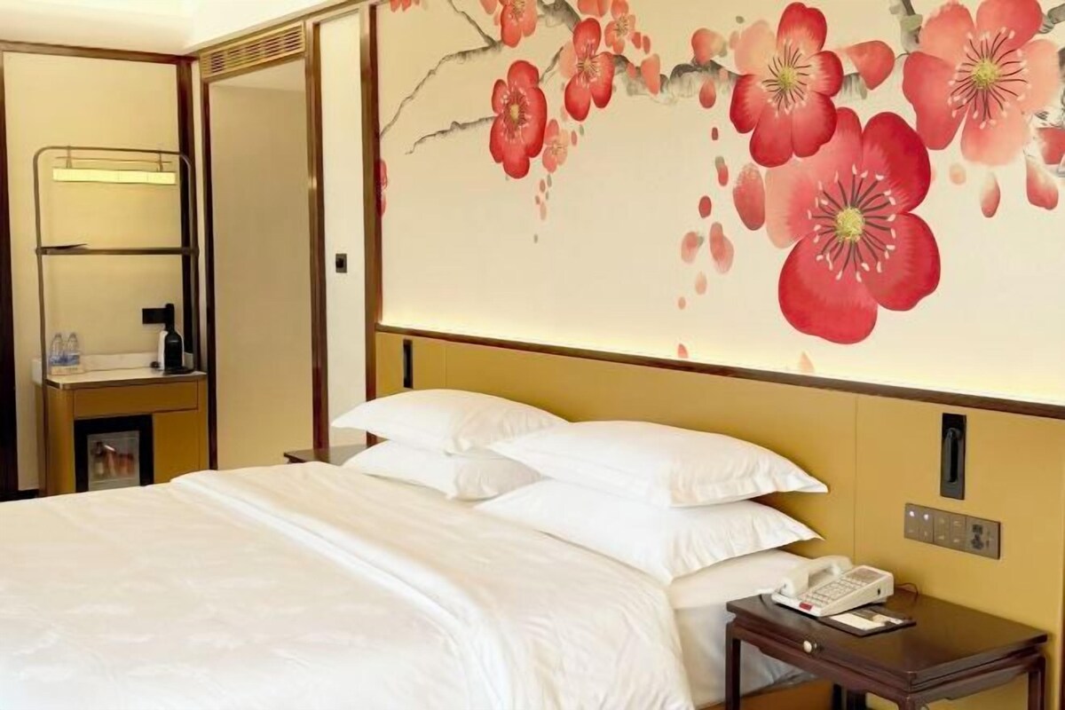 A hotel room with a bed, a bedside table with a phone, and a wall with a floral mural.