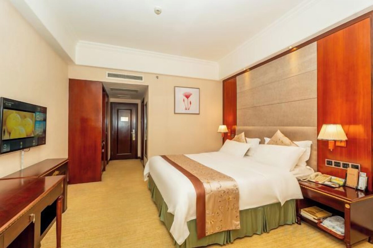 A hotel room with a large bed, bedside tables, a TV, and a door leading to another room.