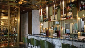 A bar area with a marble countertop, green bar stools, and shelves stocked with bottles and glasses. - Rongjiang Hotel (Jieyang)