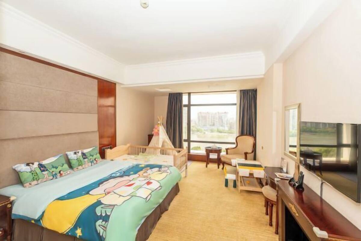 A hotel room with a large bed, a desk, a chair, a TV, and a window with a view.