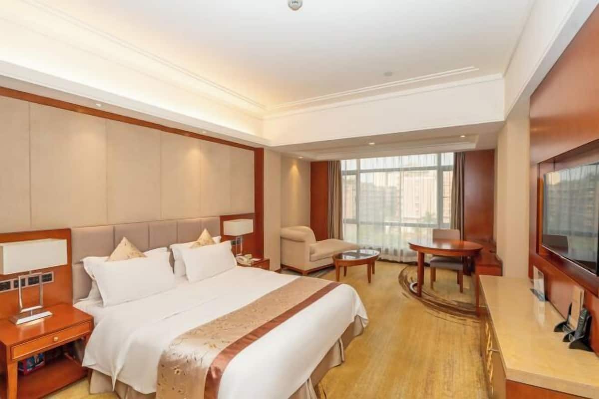 A hotel room with a large bed, a desk, a chair, and a television.