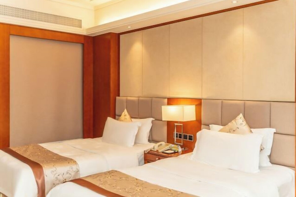 A hotel room with two beds, a wooden headboard, a nightstand with a lamp, and a telephone.