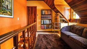 Ein gemütliches Dachzimmer mit einer Holztreppe, einem Bücherregal, einem Sofa und einem gerahmten Bild an der Wand.