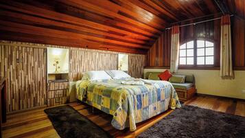 A cozy bedroom with a wooden ceiling, a bed with a colorful quilt, a nightstand, a lamp, and a window with curtains.