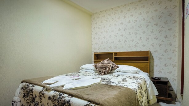 Una cama bien hecha con ropa de cama floral, un cabecero de madera y una mesita de noche con un control remoto.