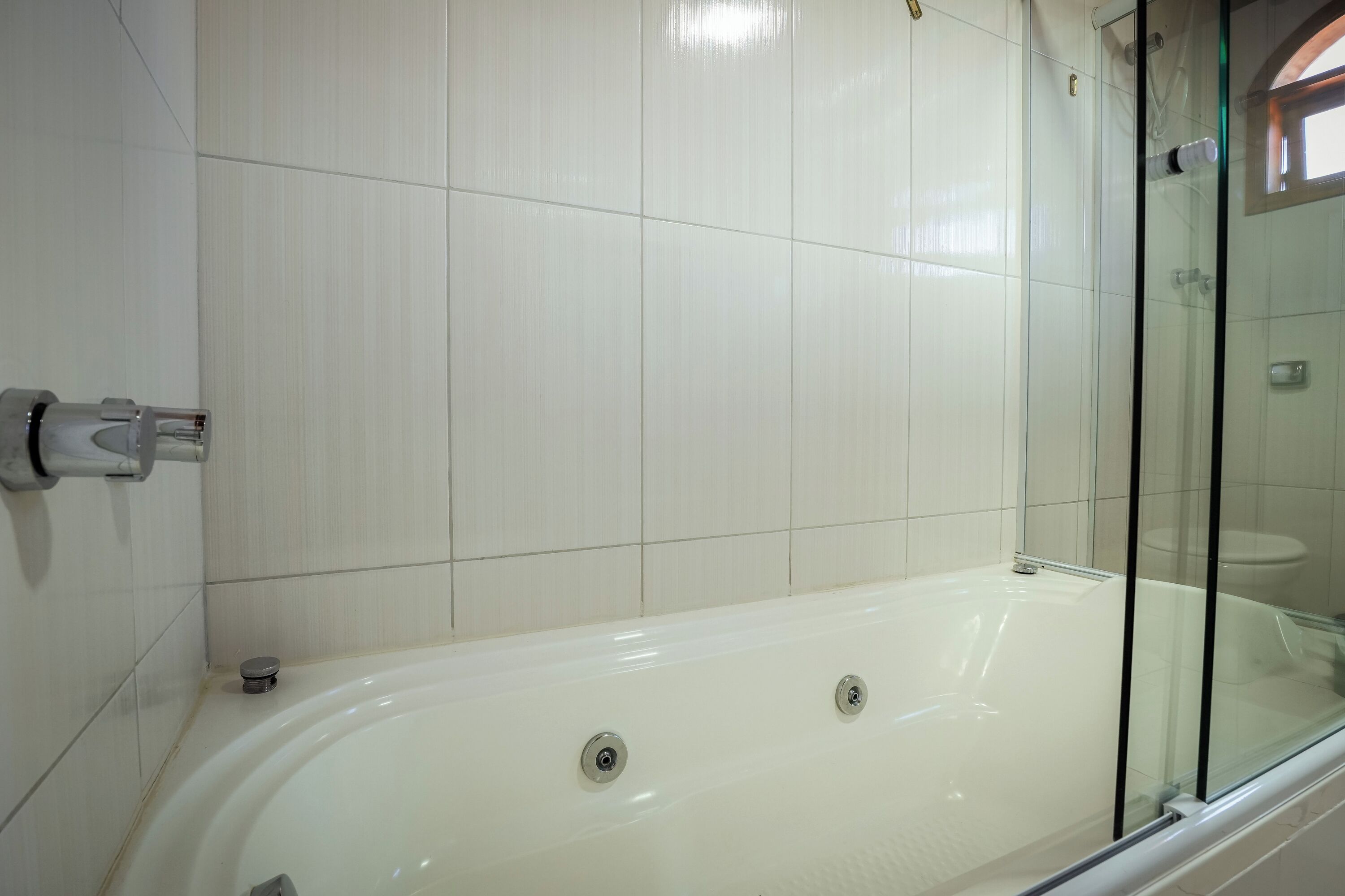A bathroom with a white bathtub, a glass shower enclosure, and white tiled walls.