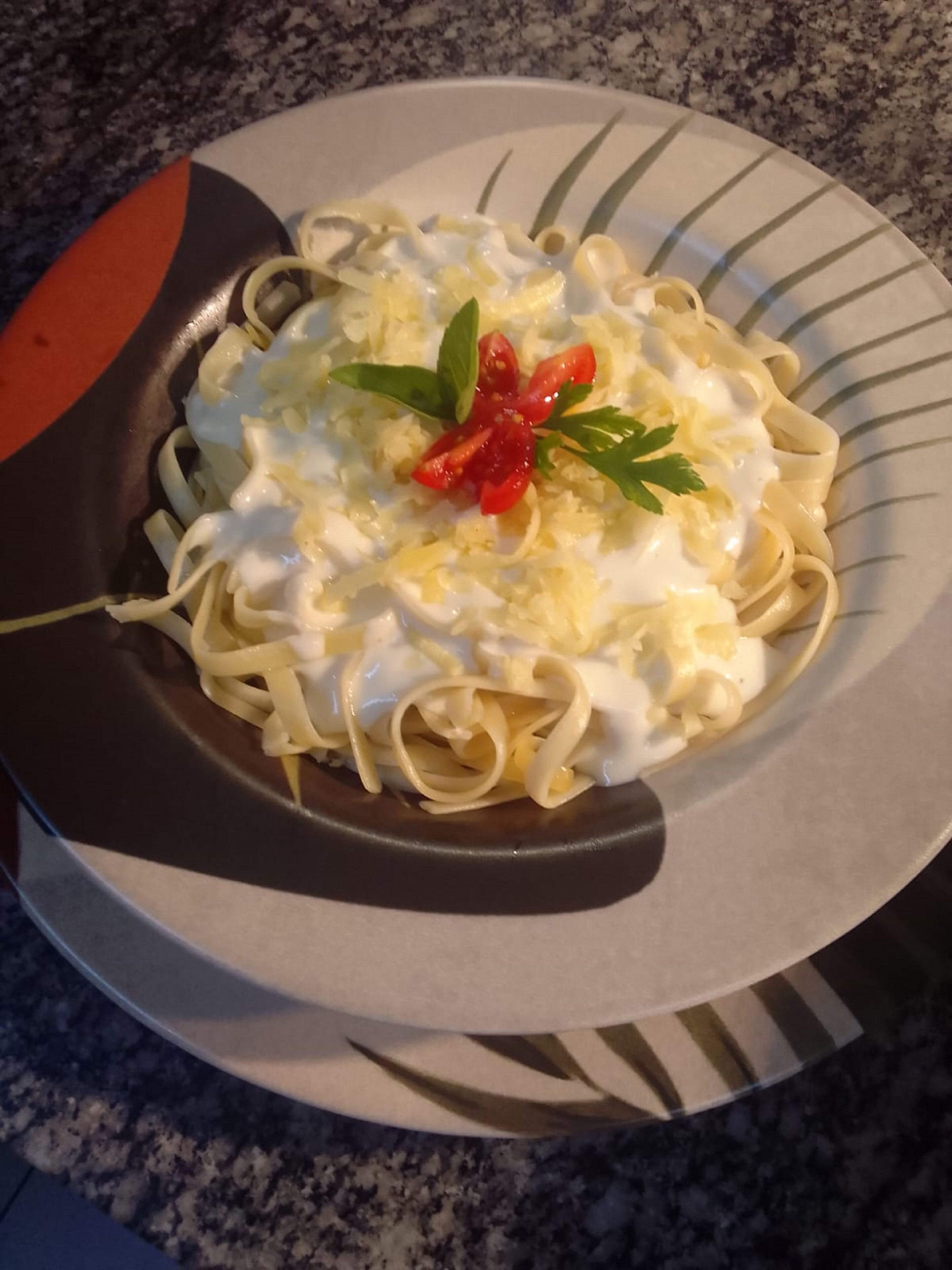 Un plato de pasta con salsa cremosa, adornado con pimiento rojo y perejil, sobre un plato a rayas.