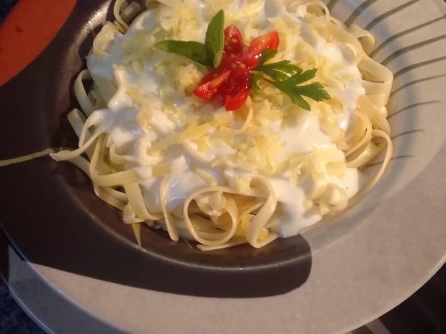 Un plato de pasta con salsa cremosa, adornado con pimiento rojo y perejil, sobre un plato a rayas.