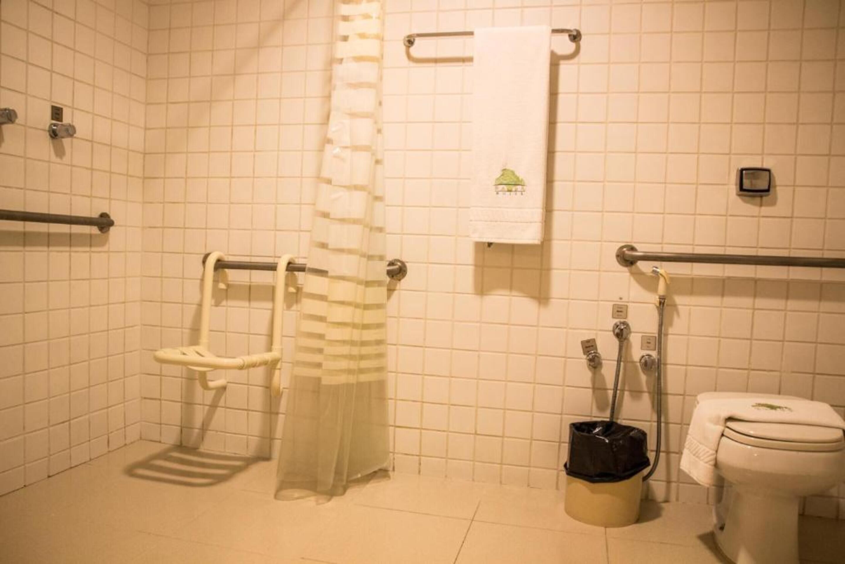 A bathroom with a toilet, a grab bar, a shower curtain, and a trash bin.