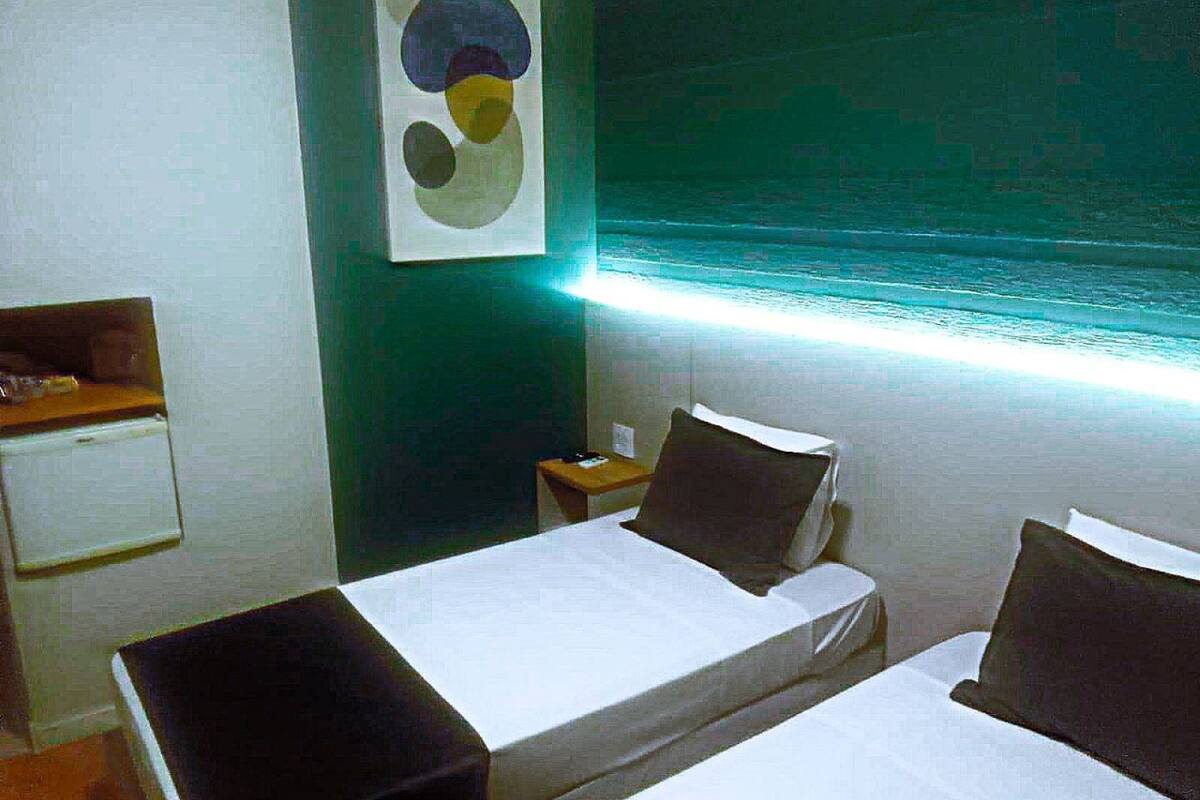 Une chambre d’hôtel avec deux lits, un petit bureau, une table de chevet et une œuvre d’art accrochée au mur.