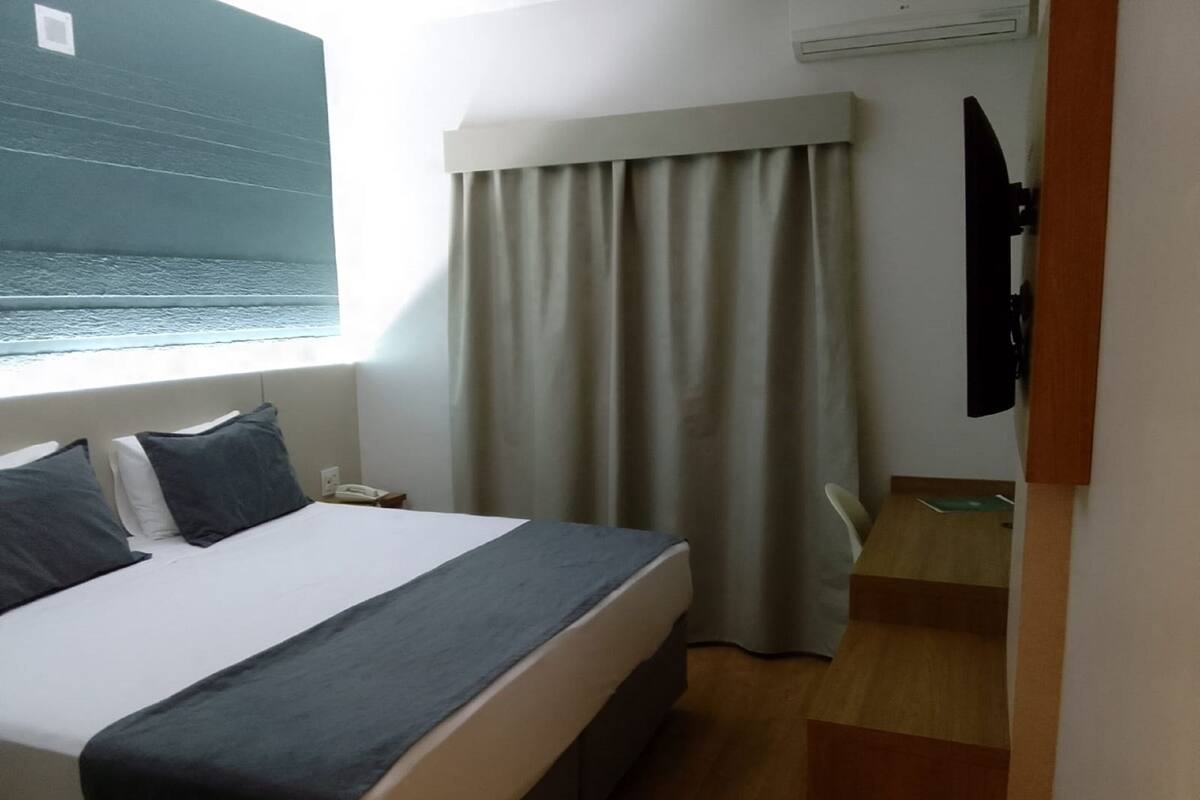 Une chambre d’hôtel avec un lit, une table de chevet, un téléphone, une fenêtre donnant sur la mer et un rideau.