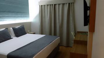 A hotel room with a bed, a bedside table, a telephone, a window with a view of the sea, and a curtain.