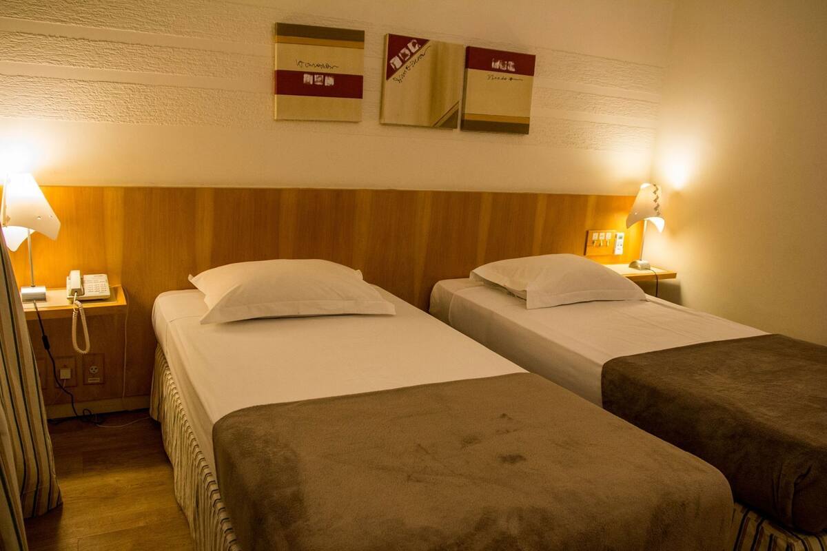 Une chambre d’hôtel avec deux lits, une tête de lit en bois, une table de chevet avec une lampe et un téléphone.
