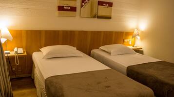 A hotel room with two beds, a wooden headboard, bedside lamps, a telephone, and framed certificates on the wall.