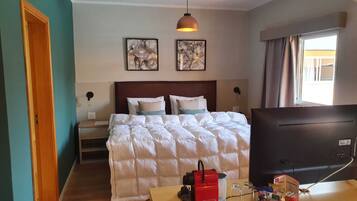Habitación de hotel con cama, televisor, escritorio y aperitivos, y dos obras de arte en la pared.