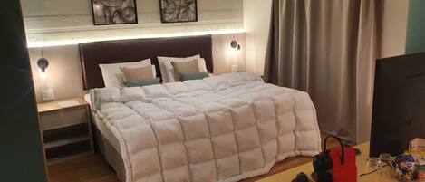 A hotel room with a large bed, a desk with a TV, and artwork on the wall.