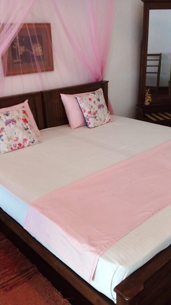 A bed with a wooden frame, two floral pillows, a pink bedspread, and a pink canopy.