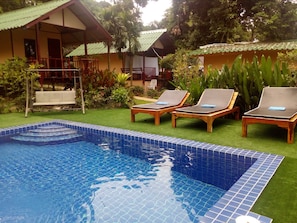 A swimming pool with tiled edges, surrounded by a grassy area with lounge chairs and a small deck. - Saint Tropez Resort (Ko Chang)