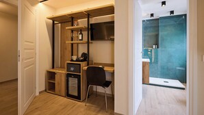 Una habitación compacta con escritorio de madera, una silla, un refrigerador pequeño y una televisión empotrada.
