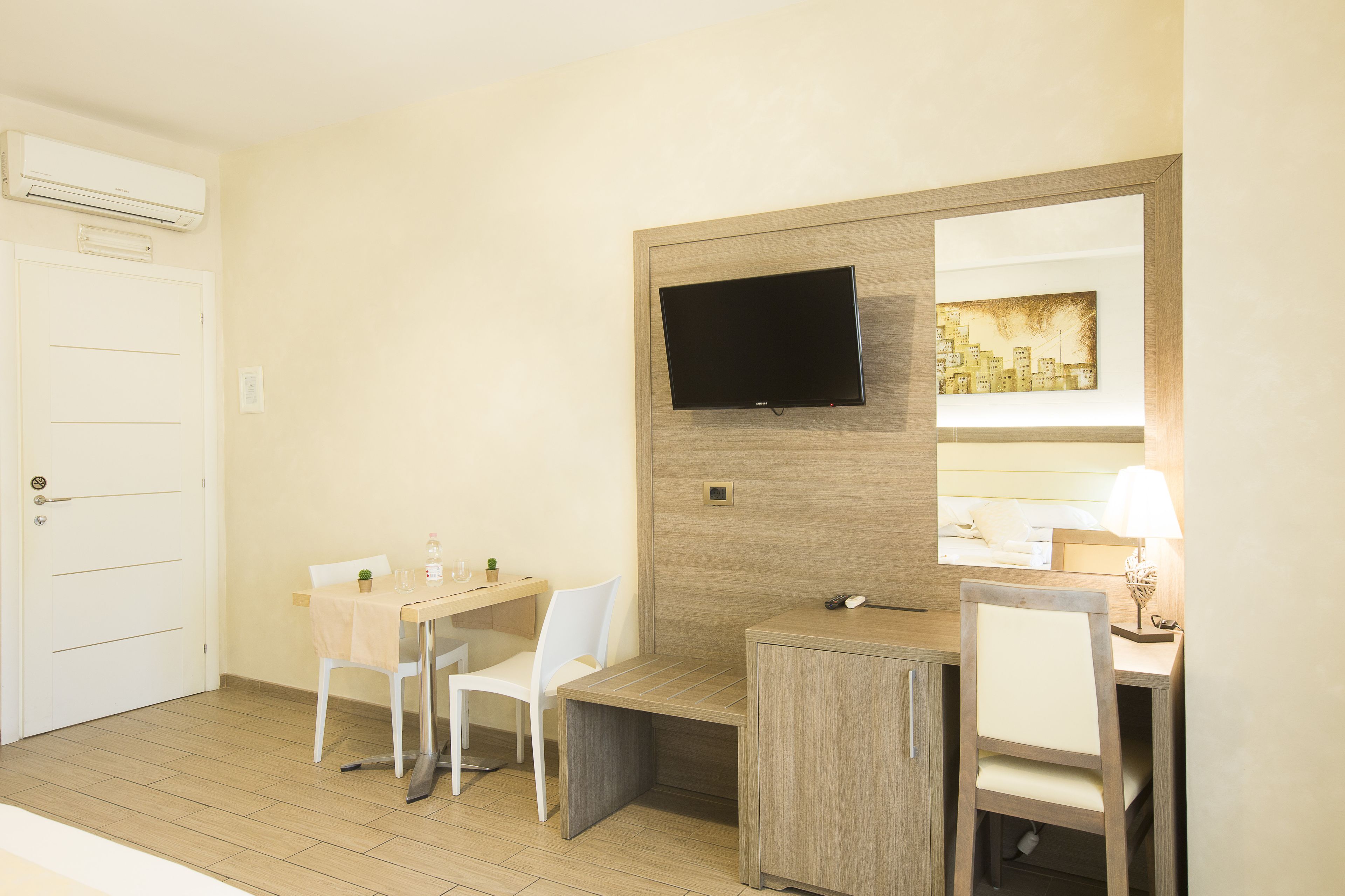 Una habitació d'hotel amb escriptori, dues cadires, televisió, mirall i llit.