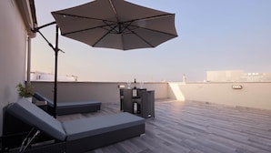 Una terraza en la azotea con una sombrilla grande, sillones de descanso y una mesita.