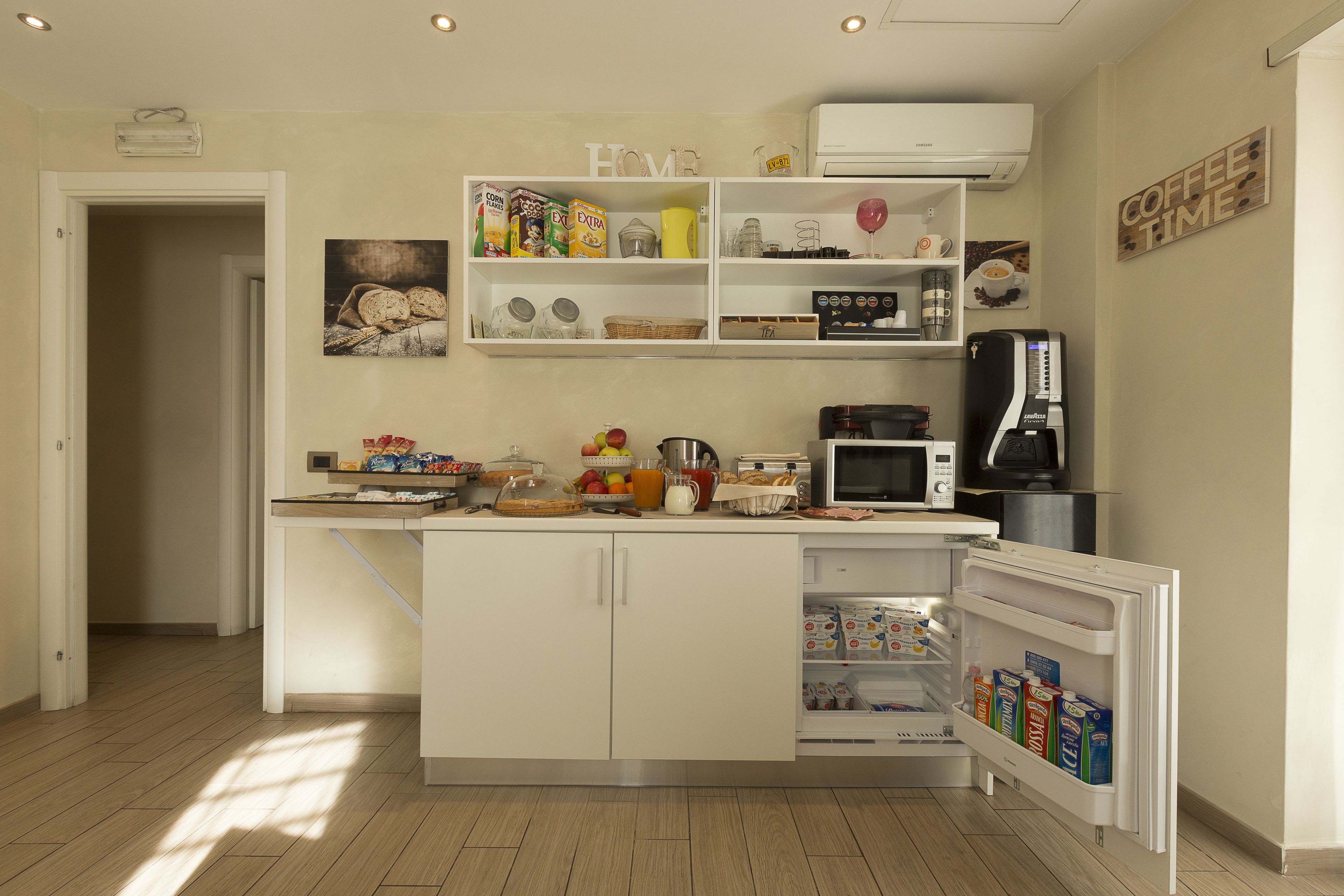 Een moderne keuken met witte kastjes, een ingebouwde magnetron, een koffieapparaat en een koelkast met een dispenser voor melk en sap.