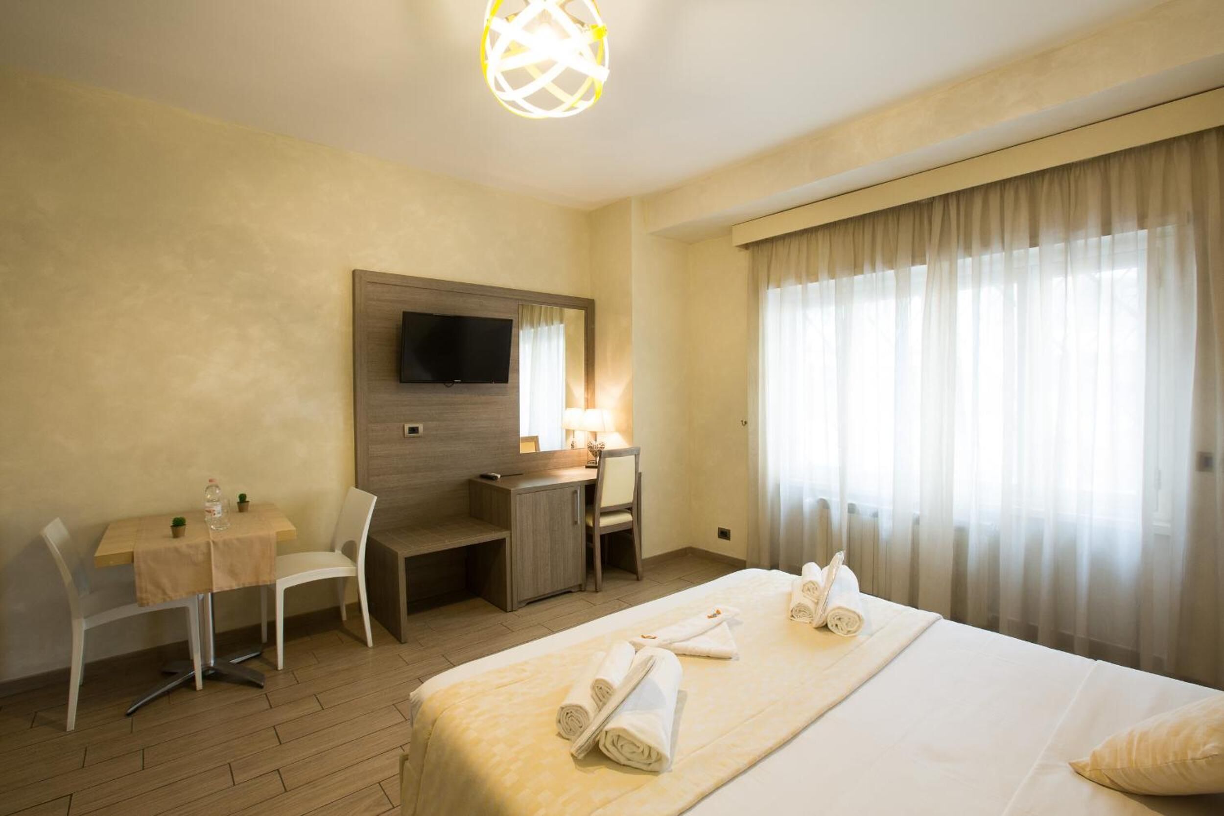 A hotel room with a bed, a desk, a chair, a TV, and a window with curtains.