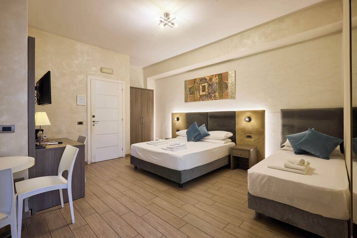 A hotel room with two beds, a desk, a chair, and a television.