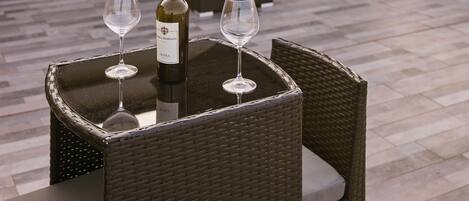 Une terrasse sur le toit avec une table dressée pour deux personnes, une bouteille de vin et deux verres. On aperçoit en arrière-plan des chaises longues et un parasol.