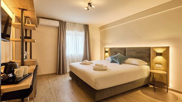 Una habitación de hotel moderna con una cama grande, mesitas de noche, un escritorio con silla y una ventana con cortinas.